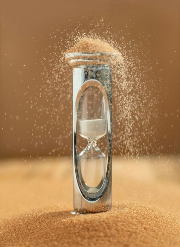 Sanduhr mit fallendem Sand auf Sandhintergrund